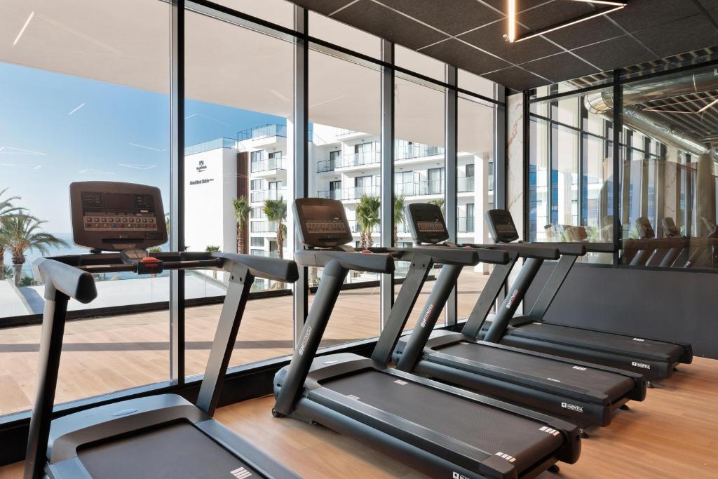 Mūsdienīgs trenažieru zāles interjers ar vairākām skrejceliņiem, kas atrodas pie lieliem logiem, caur kuriem redzama apkārtne un baseins. Gaisīga un moderni iekārtota telpa, kas veicina aktīvu dzīvesveidu.