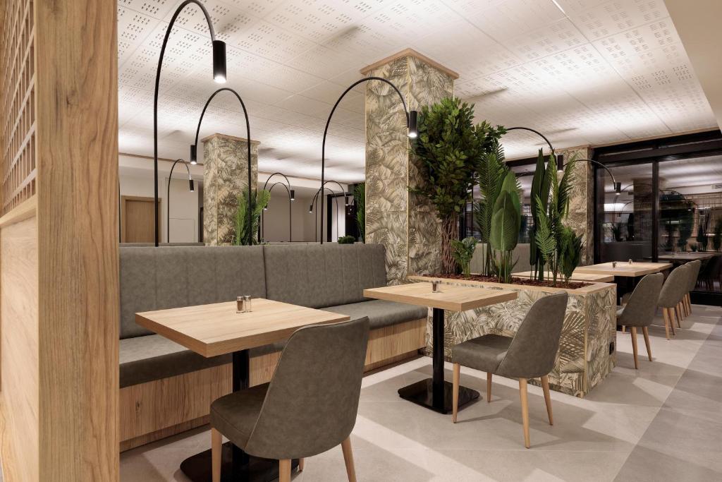 Mūsdienīgs restorāna interjers ar ērtām sēdvietām, koka akcentiem un zaļām augiem, kas rada patīkamu atmosfēru. Gaismas elementi un eleganta dizaina detaļas papildina kopējo noskaņu.