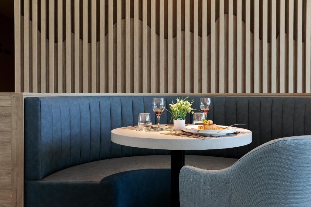 Mūsdienīgs restorāna stūrītis ar ērtu sēdvietu, elegantu galdu un izsmalcinātu maltīti, ko rotā ziedi un vīna glāzes.