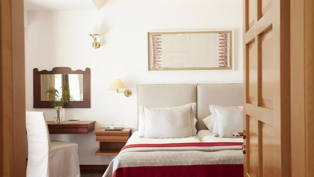 Mūsdienīgs guļamistabas interjers ar gultu, spilveniem un elegantu piekārtu mākslas darbu, blakus atrodas rakstāmgalds un spogulis. Gaismas un krāsu kombinācija rada mierīgu atmosfēru.