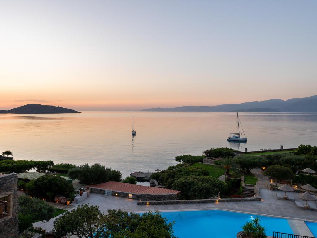 Saulrieta skats pār mierīgu jūru ar laivu un kalnainu fona ainavu. Daba un klusums rada relaksējošu atmosfēru.