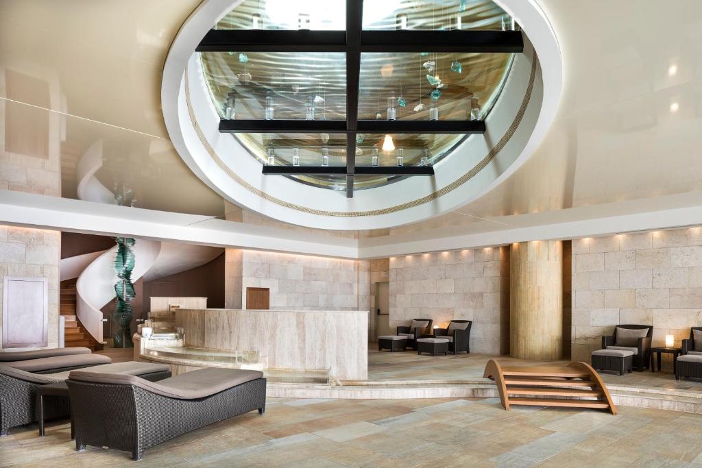 Mūsdienīgs spa un atpūtas telpas interjers ar elegantu dizainu, kas ietver stikla griestus un komfortablus atpūtas krēslus. Telpa ir gaiša un plaša ar dabīgām akmens sienām un elegantiem aksesuāriem.