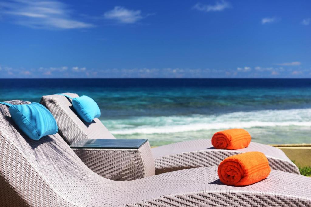 Atpūtas krēsli ar ziliem spilveniem un oranžām dvieļu ruļļiem, skats uz jūru un skaidru zilo debesu fonā.