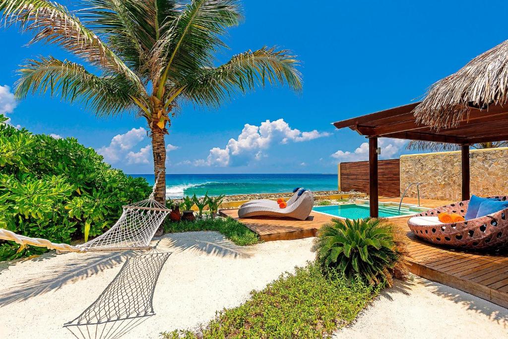 Tropu pludmales ainava ar palmām, peldbaseinu un ērtiem atpūtas krēsliem, ideāla relaksācijai pie jūras. Skats uz zilo okeānu un baltās smiltis rada mierīgu atmosfēru.