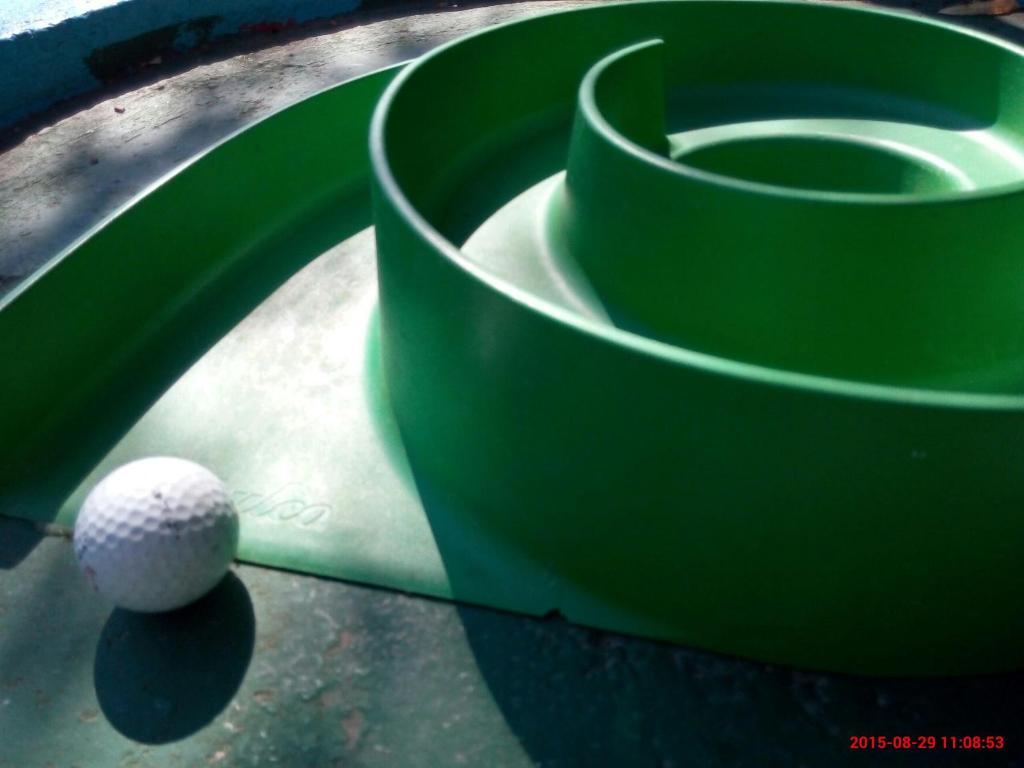 Zaļš spirālveida laukums ar balto golfa bumbiņu tuvplānā, kas atrodas blakus spirāles malai.