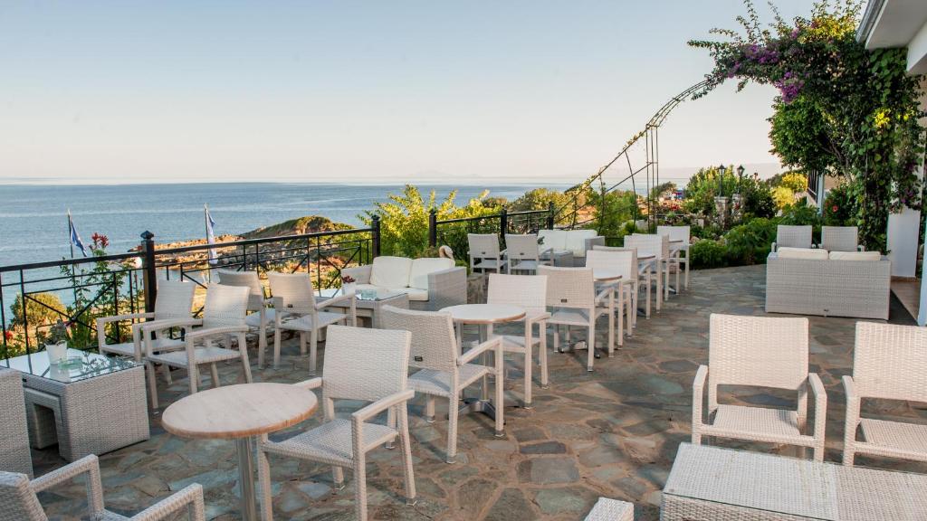 Terases zona ar baltiem mēbeļu komplektiem un panorāmas skatu uz jūru, ideāla relaksācijai un atpūtai. Ziedi un zaļumi papildina ainavu.