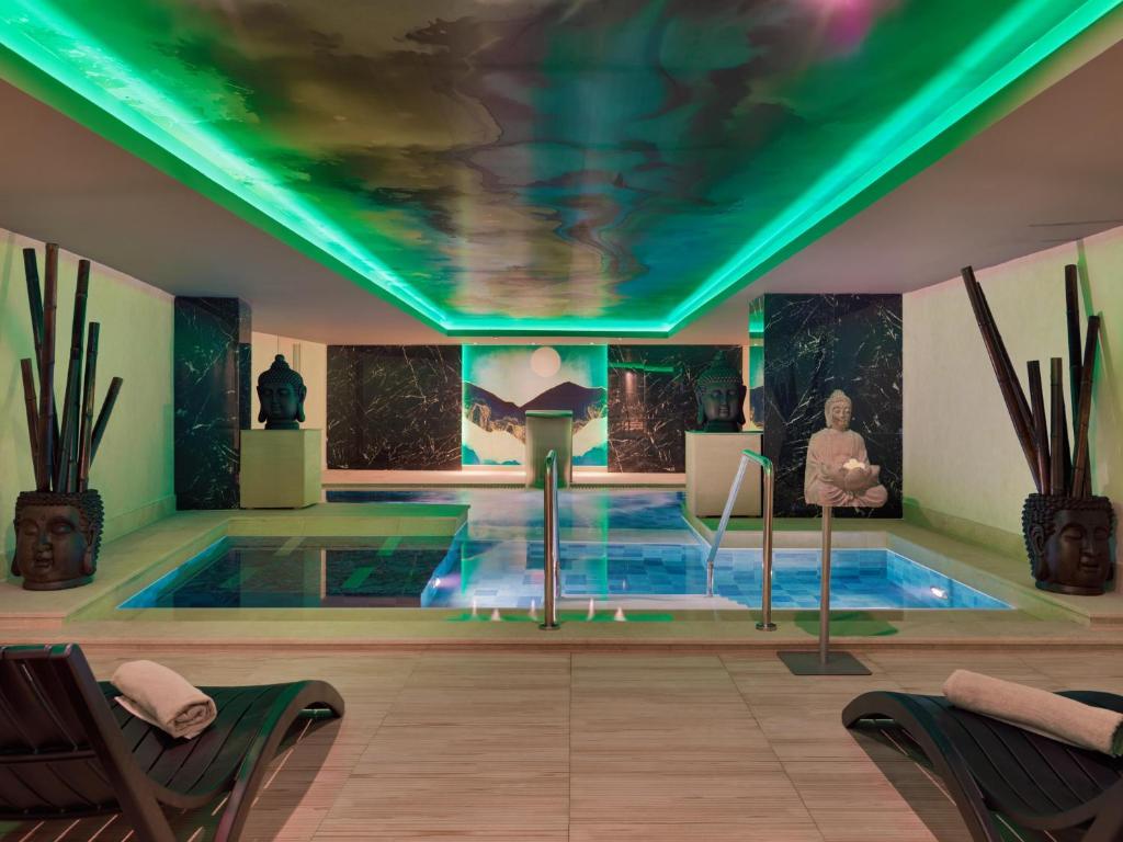 Mūsdienīgs spa interjers ar relaksējošu atmosfēru, ietverot baseinu, skulptūras un zaļganu apgaismojumu. Ideāla vieta atpūtai un relaksācijai.