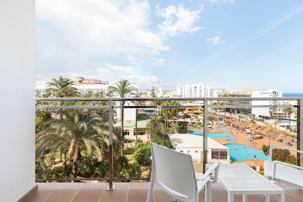 Skats no balkona uz viesnīcu ar baseinu, palmām un debesskrāpjiem fona. Ideāls atpūtas brīdis saulainā dienā.