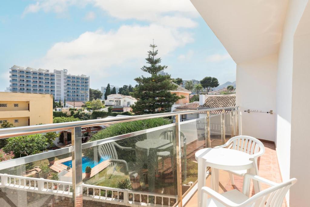 Skats no balkona uz pilsētas ainavu, kur redzami dzīvojamie nami un baseins dārzā. Gaismas un zaļuma pieskāriens rada relaksējošu atmosfēru.