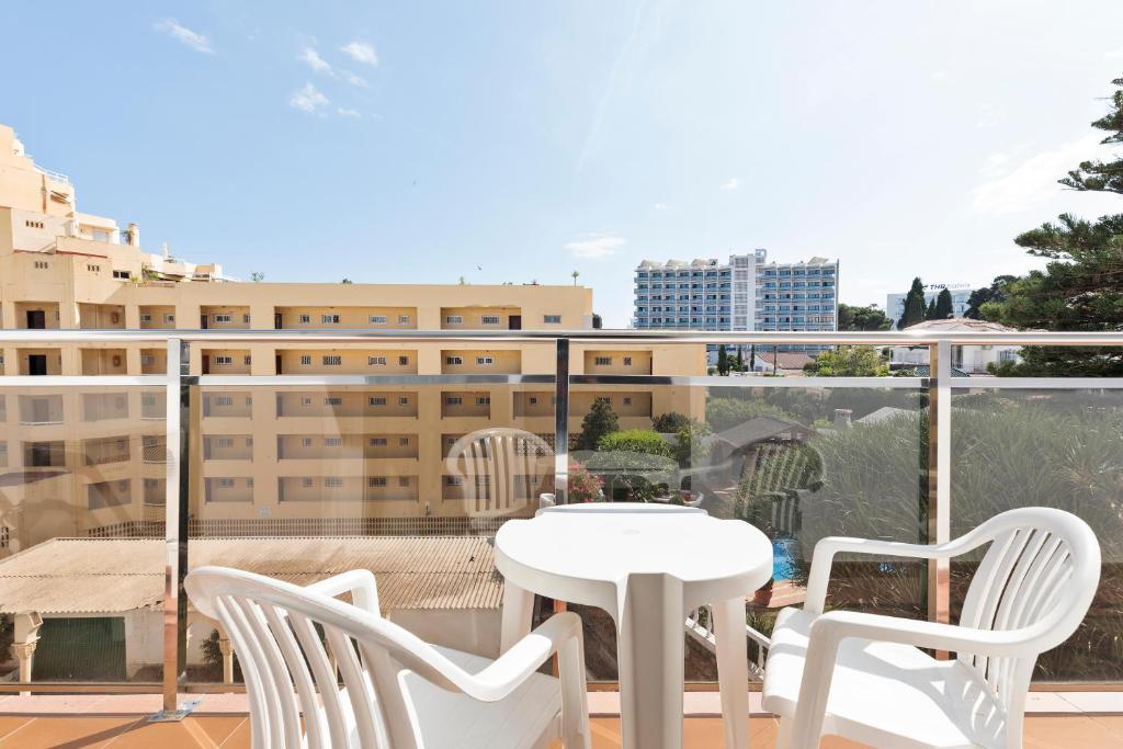 Balkona skats ar baltām plastmasas krēsliem un galdu, redzami apkārtnes ēku un zaļumi.