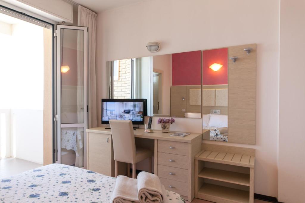 Mūsdienīga viesnīcas numura interjers ar gultu, rakstāmo galdu un televizoru, kā arī lieliem logiem, kas ved uz balkonu. Uz galda ir ziedu kompozīcija un grāmatas.