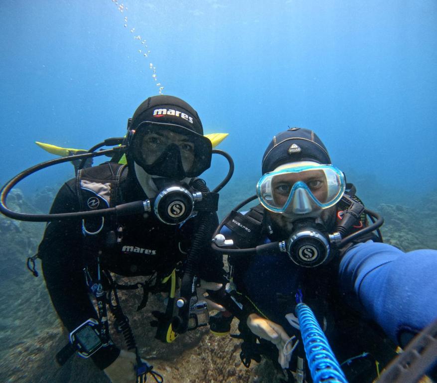 Divers posing underwater, equipped with scuba gear and masks, surrounded by a clear blue ocean.