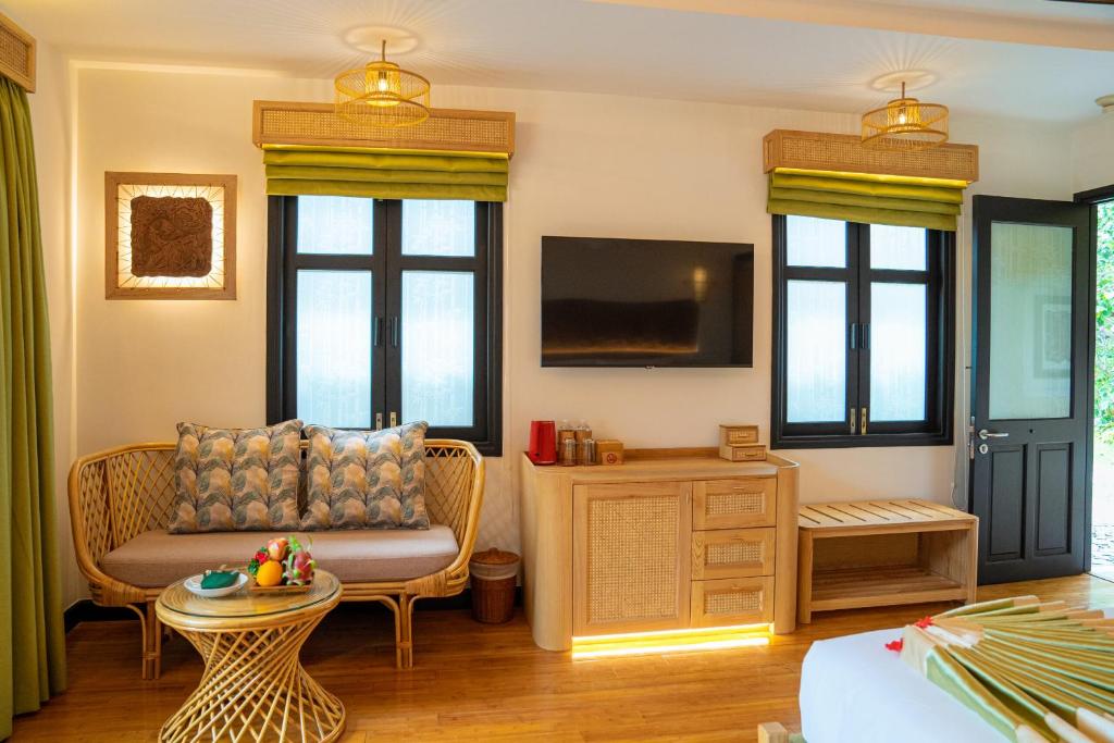 Mūsdienīgs viesnīcas numurs ar ratanā izgatavotu dīvānu, dekoratīviem spilveniem un koka mēbelēm. Telpā ir televizors un gaiši logi ar zaļām žalūzijām, radot patīkamu un ērtu atmosfēru.