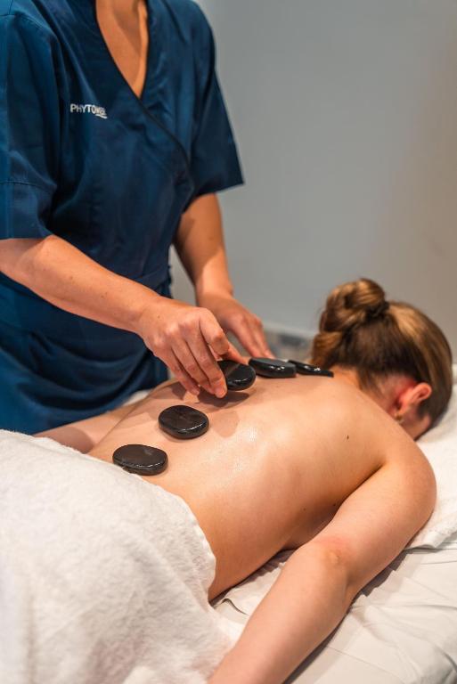 Masāžas sesija ar karstajiem akmeņiem, kur terapeits uzklāj akmeņus uz klienta muguras relaksējošai ārstēšanai.