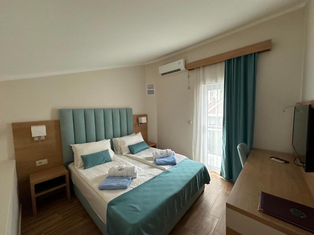 Mūsdienīga viesnīcas numura interjers ar divām gultām, koka mēbelēm un palagiem, kas rotāti ar zilu dekoru. Logi ar aizkariem nodrošina dabisko apgaismojumu.