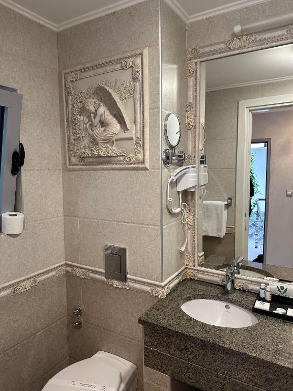 Vannas istaba ar elegantu dekoru, kas ietver reljefu attēlu uz sienas, spoguli un mūsdienīgu izlietni. Svarīgi elementi ir arī higiēnas piederumi un viesnīcas pakalpojumi.