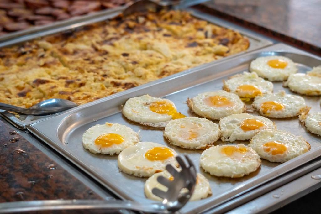 Fried eggs are neatly arranged on a tray, showcasing golden yolks, alongside a baked dish in the background. Perfect for a hearty breakfast spread.