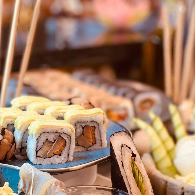 Svaigu sushi uzkodu assortments ar dažādām sastāvdaļām un krāsainām garnējumiem, pasniegts uz zilo šķivīti.