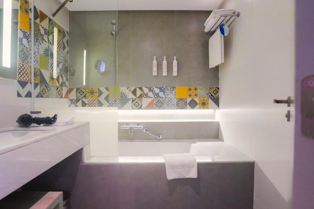 Moderns vannas istabas interjers ar krāsainām flīzēm, dušas kabīni un vannu. Uz galda ir fēns un dvielis, radot mājīgu atmosfēru.