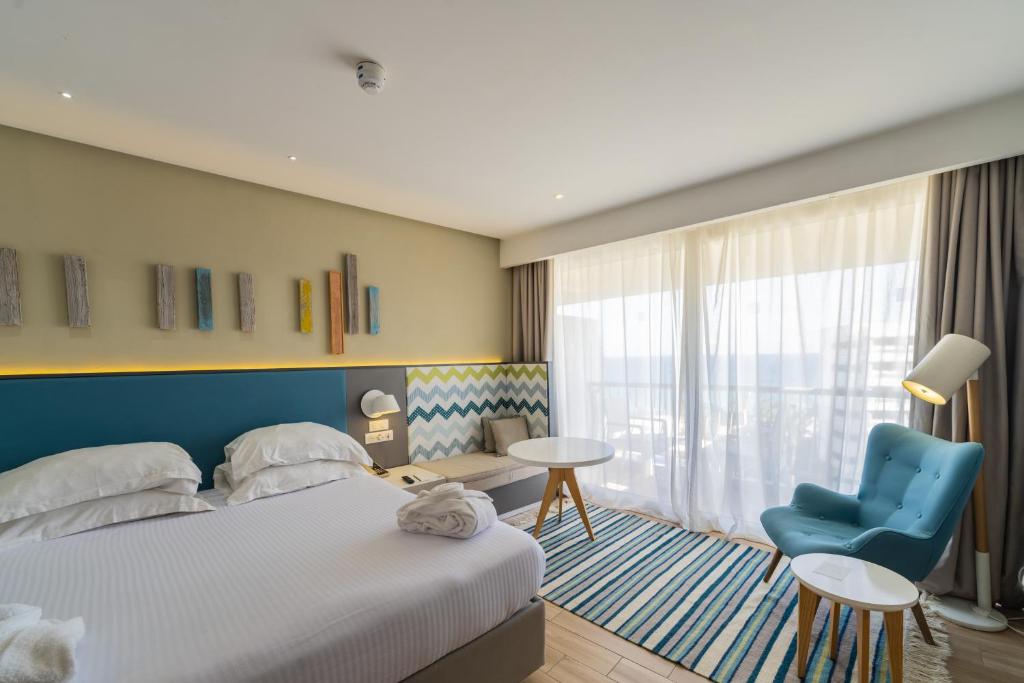 Mūsdienīgs viesnīcas numurs ar gultu, dzīvojamo zonu un plašiem logiem, caur kuriem ieplūst dabiska gaisma. Interjers ir veidots ar krāsainiem akcentiem un stilīgu mēbeļu dizainu.