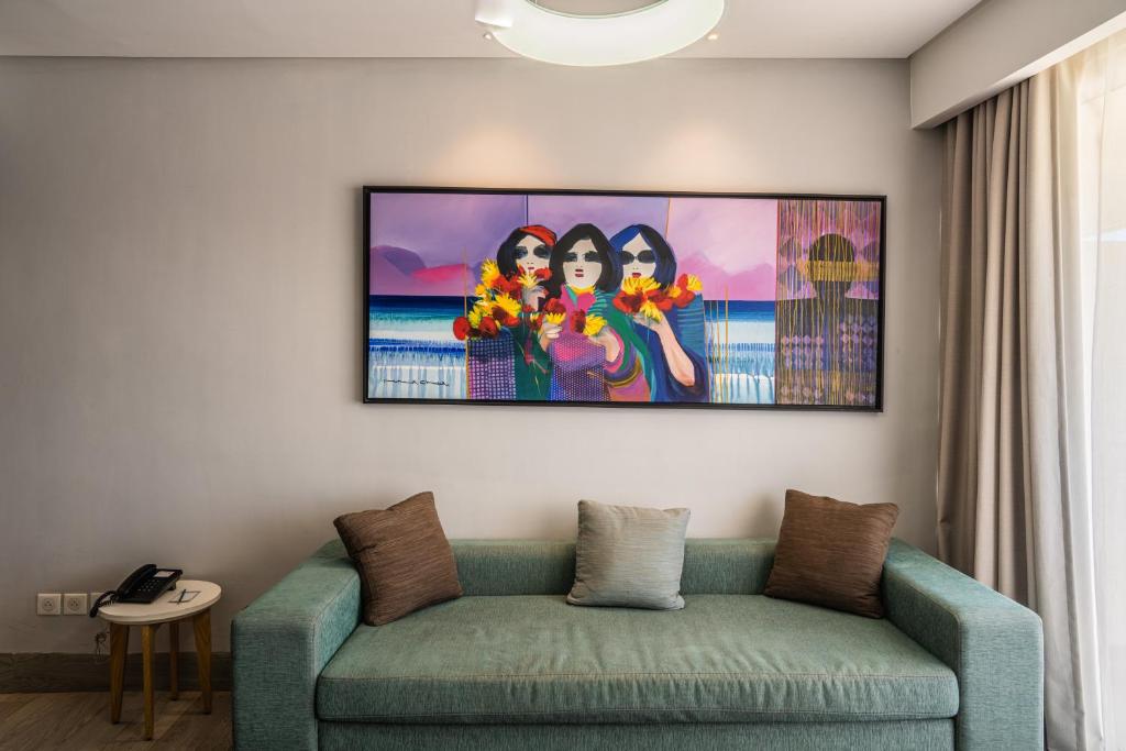 Mūsdienīga telpa ar krāsainu gleznu, kurā attēlotas trīs sievietes ar ziediem rokās, un dīvāns ar spilveniem. Glezna piešķir dzīvīgumu un mājīgumu interjeram.