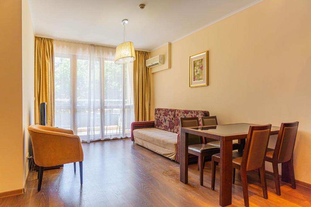 Mūsdienīgs viesistabas interjers ar dīvānu, ēdamgaldu un krēslu komplektu, gaišām sienām un logiem ar aizkariem. Telpā ir arī gaismeklis un gaisa kondicionieris.