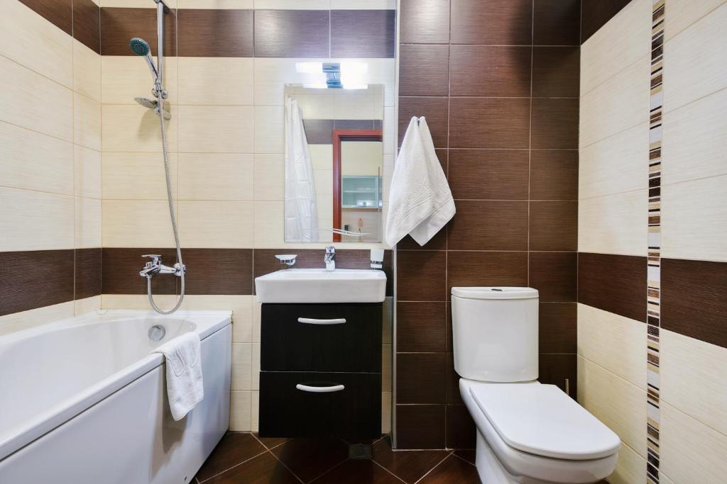 Mūsdienīgs vannas istabas interjers ar vannu, izlietni un tualeti, akcentēts ar brūnu un bēšu flīzēm. Eleganta spogulis un higiēnas piederumi pieejami.