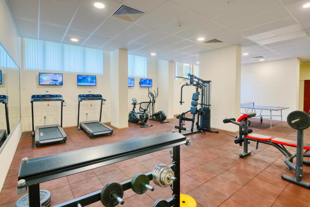 Mūsdienīga trenažieru zāle ar dažādām iekārtām, tostarp skrejceliņiem, velotrenažieriem un svaru staciju, apgaismota ar dabiskiem gaismas avotiem un televizoriem.