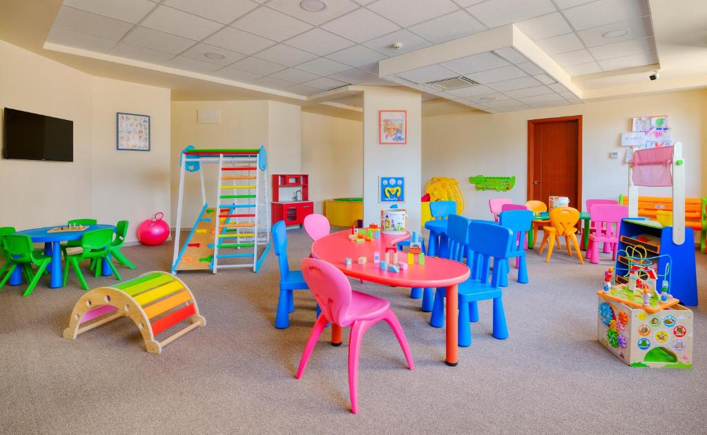 Krāsaina bērnu spēļu istaba ar daudzveidīgu mēbeļu un rotaļlietu klāstu, kas iepriecina bērnus. Telpa ir aprīkota ar galdiem, krēsliem un rotaļu elementiem, kas veicina radošu mācīšanos un spēles.