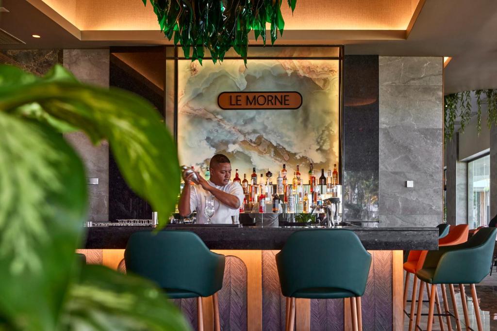 Elegantā bāra interjers ar viesmīli, kurš gatavo kokteiļus. Fons rotā aksesuāri un mūsdienīgs dizains, radot patīkamu atmosfēru.