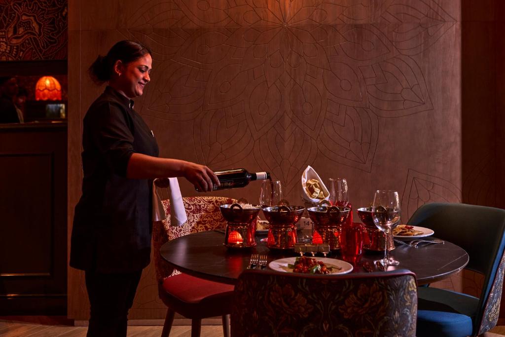Viesmīlis apkalpo viesus, ielejot vīnu elegantā restorānā ar izsmalcinātu galdu, kas ir noformēts ar gardām maltītēm un stilīgām glāzēm.
