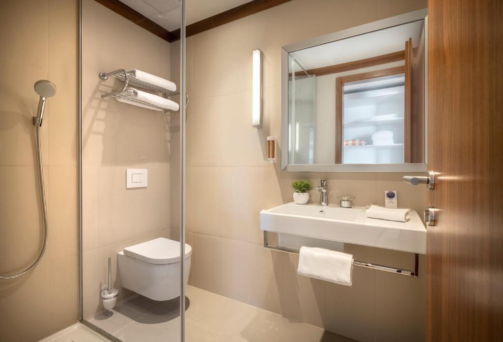 Mūsdienīga vannas istaba ar dušu, piekārtiem dvieļiem un modernu izlietni, kas nodrošina elegantu un tīru atmosfēru. Ideāli piemērota relaksējošai pieredzei.