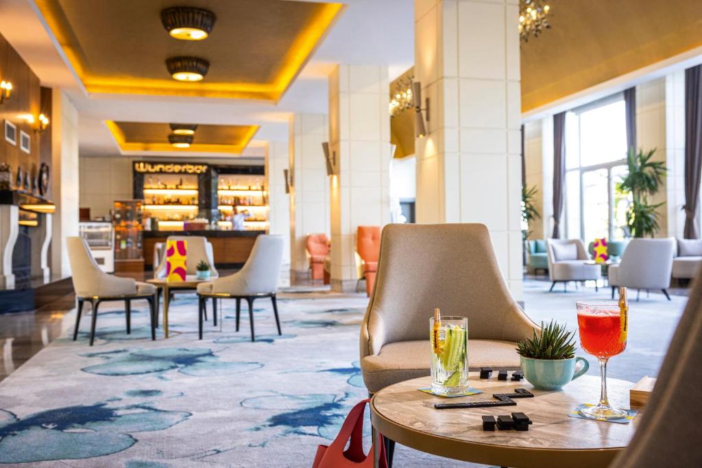 Elegants viesnīcas interjers ar modernām mēbelēm un krāsainiem kokteiļiem uz galda, radot relaksējošu atmosfēru. Pamatā ir gaišas krāsas un izsmalcināta apgaismojuma kombinācija.