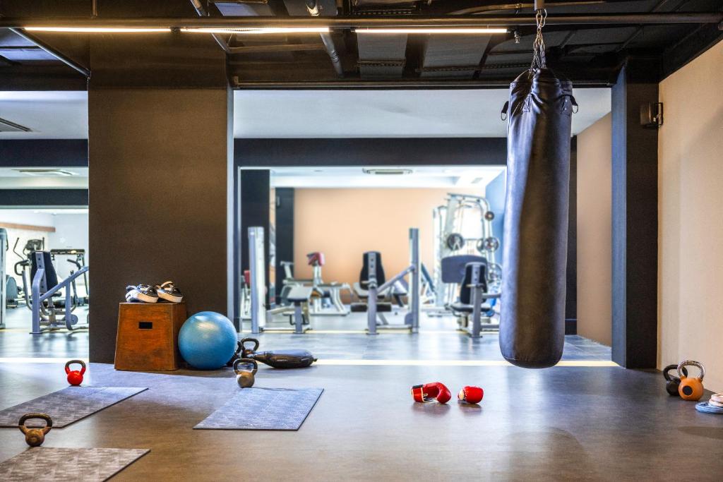 Mūsdienīgs sporta zāles interjers ar treniņu aprīkojumu, ieskaitot hanteles, sporta bumbu un boksa maisu. Fons norāda uz dažādiem trenažieriem un treniņu matiem.