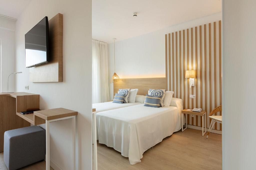 Mūsdienīgs guļamistabas interjers ar divām gultām, koka akcentiem un televizoru pie sienas. Telpā ir gaišas krāsas un minimālistisks dizains, radot patīkamu un relaksējošu atmosfēru.