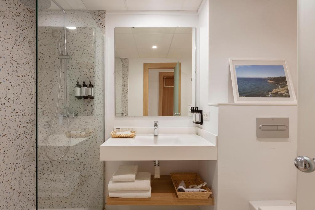 Mūsdienīgs vannas istabas interjers ar dušas stūri, elegantu spoguli un minimālistisku izskatu. Uz galda ir aksesuāri un dvieļi, radot viesmīlīgu atmosfēru.