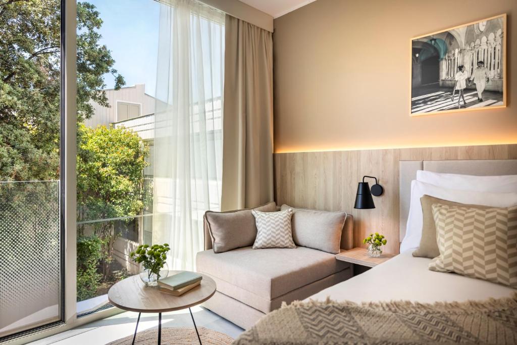 Mūsdienīgs viesnīcas numurs ar lieliem logiem, kas piedāvā skatu uz dārzu. Numurā ir ērtas mēbeles, gaismas un mākslas darbs uz sienas, radot patīkamu atmosfēru.