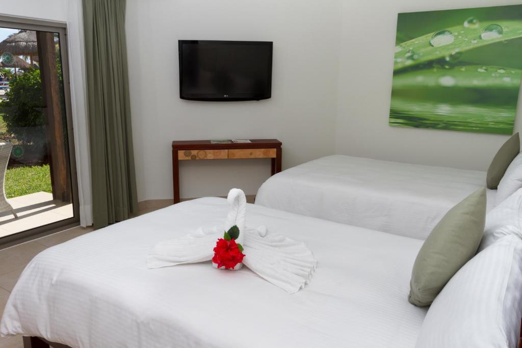 Mūsdienīga viesnīcas numura iekārtojums ar divām gultām, televizoru un dekoratīvu gulēšanas pūci ar ziedu. Interjers ir gaišs un svaigs, ar skatu uz dārzu.