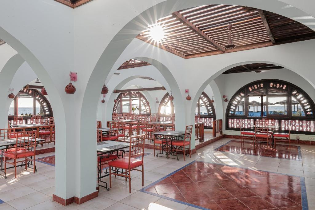 Gaišs un plašs restorāns ar arku stiliem un sarkaniem krēsliem, kurā caur logiem ieplūst saules gaisma. Interjers rada viesmīlīgu atmosfēru, ideāli piemērotu ēšanai un atpūtai.
