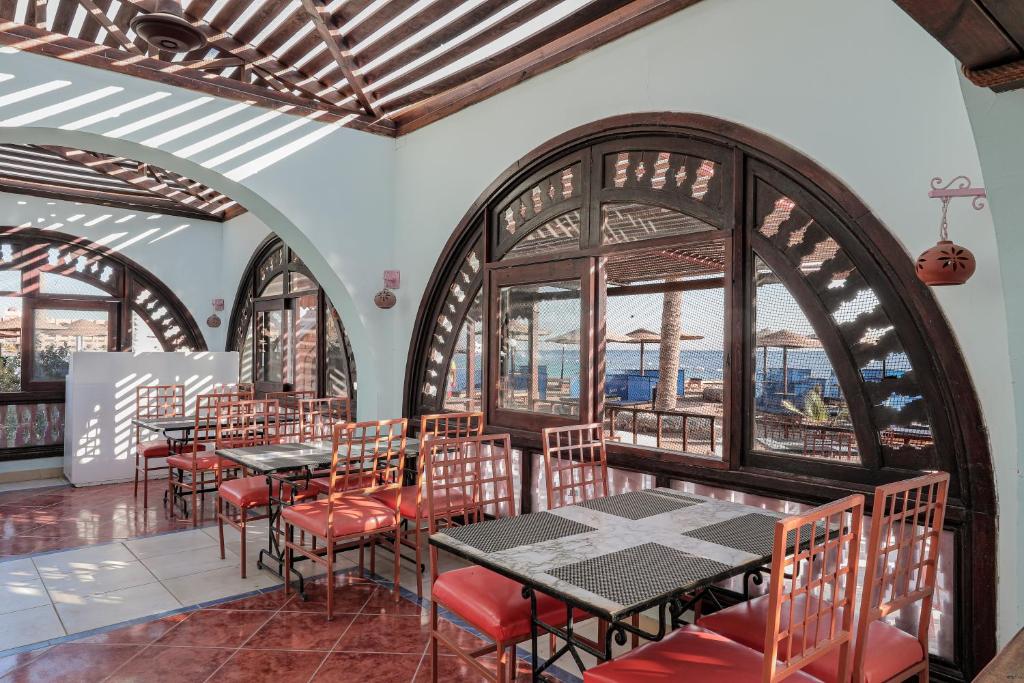 Restorāna interjers ar arku formas logiem un sarkanām krēsliem, kas piedāvā skatu uz jūru. Gaisma plūst caur koka žogiem, radot patīkamu atmosfēru.
