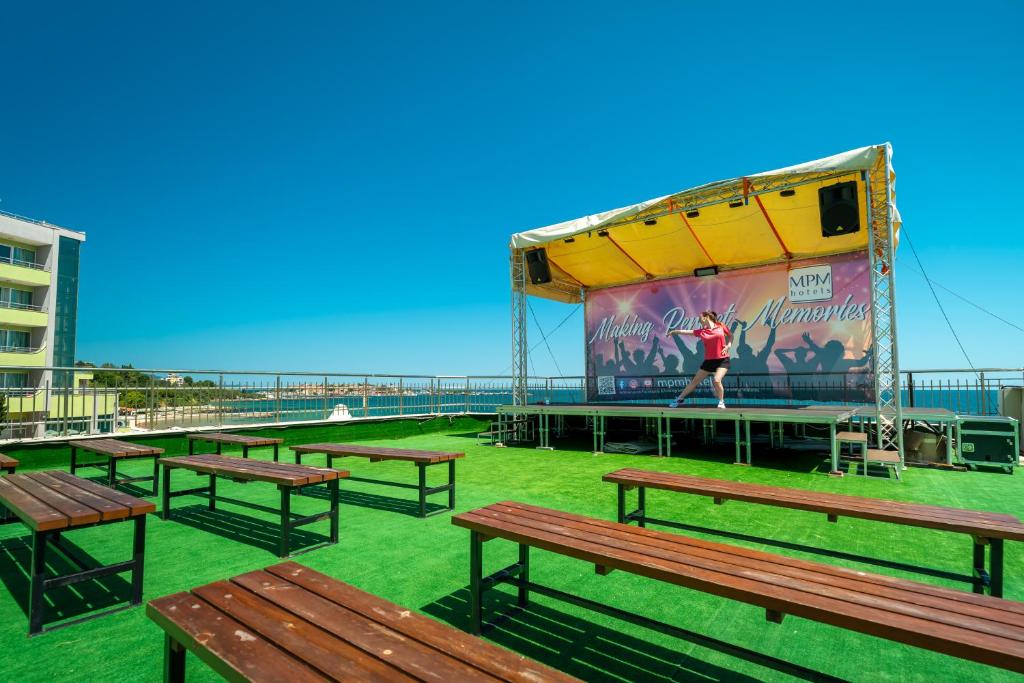 Skatuve ar izpildītāju un kafejnīcas galdiem uz jumta, ar jūras skatu un skaidru zilu debesu fonu.