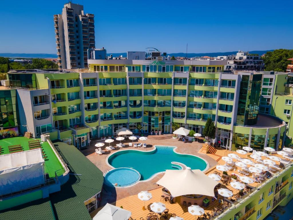 Viesnīca ar modernu arhitektūru un peldbaseinu, ko ieskauj sauļošanās krēsli un ēdamzonas. Zaļas ēkas fasāde un skats uz apkārtējo ainavu.