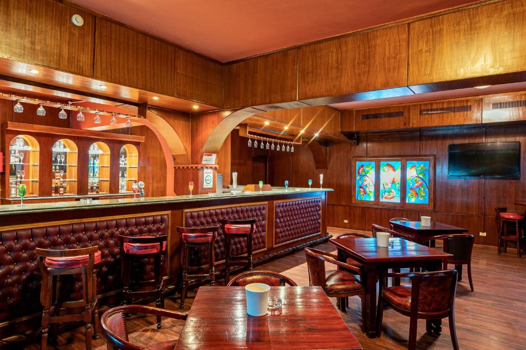 Klasisks bārs ar koka interjeru, stilīgu apgaismojumu un krāsainiem vitrāžas logiem. Vairāki galdi un krēsli, kas aicina uz relaksāciju un socializēšanos.