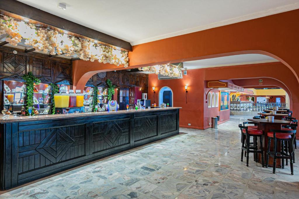 Mūsdienīgs bārs ar elegantu melnu galdu un krāsainu apgaismojumu, kas rada viesmīlīgu atmosfēru. Interjers ietver dekoratīvus elementus ar zaļumu un stilīgām mēbelēm.