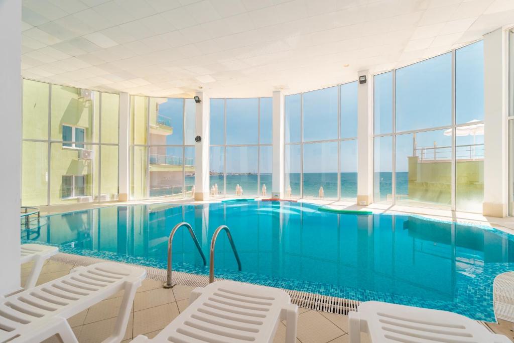 Iekštelpu peldbaseins ar skatu uz jūru, apgaismots ar dabiskiem saules stariem un apjozts ar guļamkrēsliem.