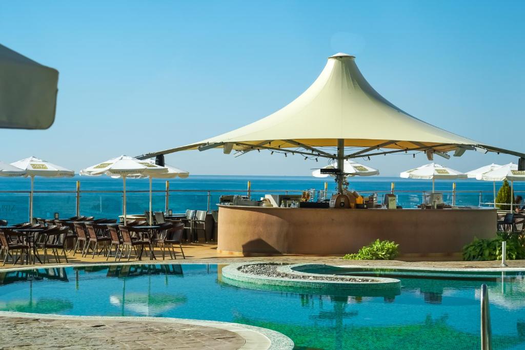 Vasaras atpūtas vieta ar peldbaseinu un bāru, kas atrodas blakus jūrai. Terase aprīkota ar saulessargiem un krēslām, radot relaksējošu atmosfēru.