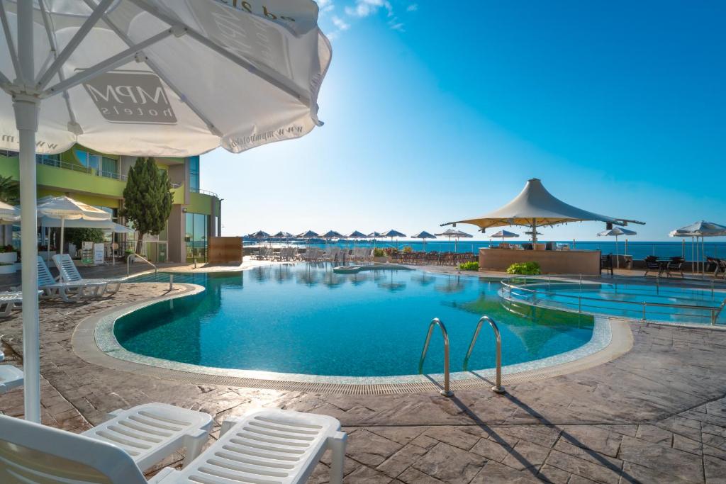 Peldbaseins ar saules gultām un lietus aizsargiem, blakus pludmalei un zilo debesu fons. Ideāla vieta atpūtai un relaksācijai.