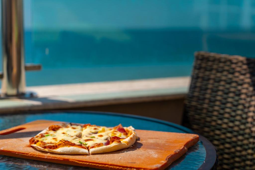 Svaigi cepta pica uz koka dēlīša, novietota uz stikla galda ar skatu uz jūru.