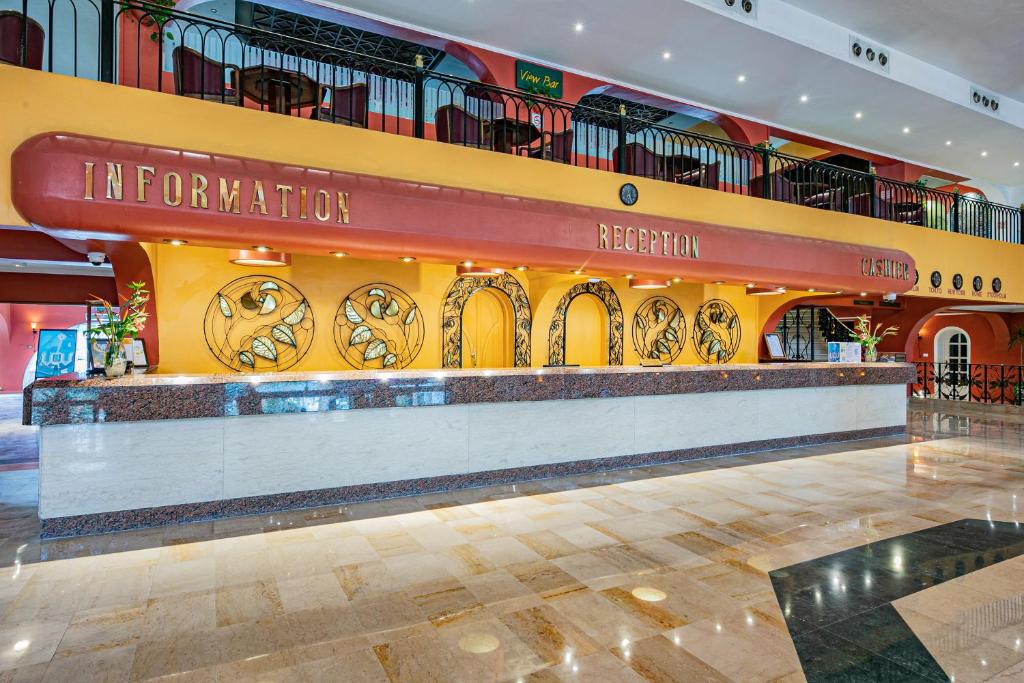 Reģistratūra viesnīcā ar krāsainu interjeru un modernu dizainu, kurā ir informācijas stends un dekoratīvi elementi. Šī telpa piedāvā viesiem siltu un laipnu atmosfēru.