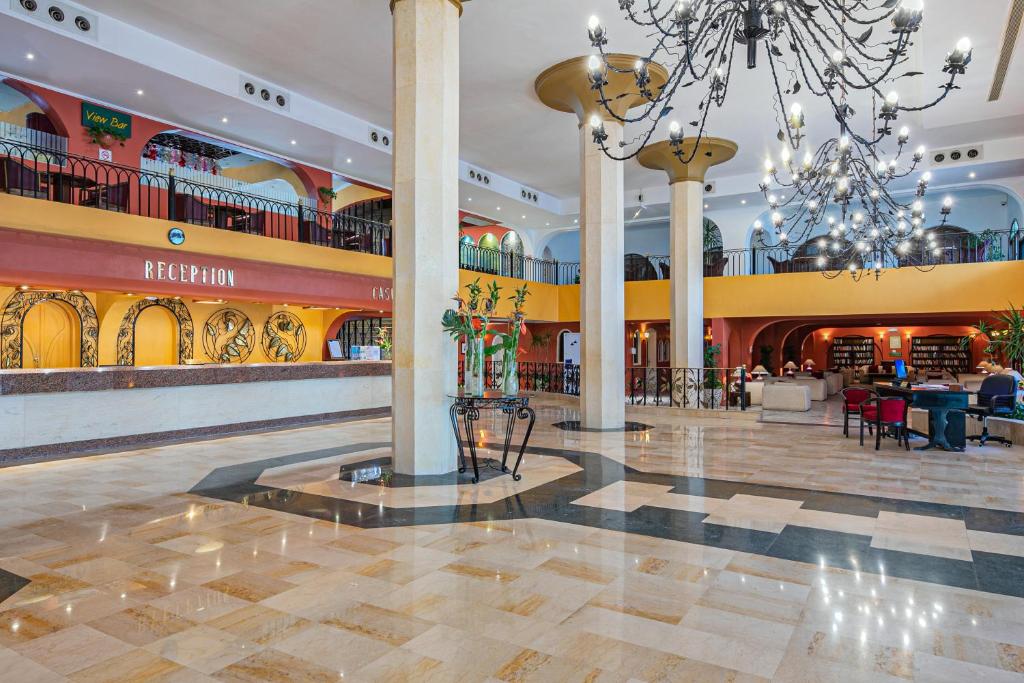 Lieliska viesnīcas reģistratūras zona ar elegantu apgaismojumu un plašām telpām. Šeit redzama moderna interjera dizaina kombinācija ar siltām krāsām un patīkamām atpūtas zonām.